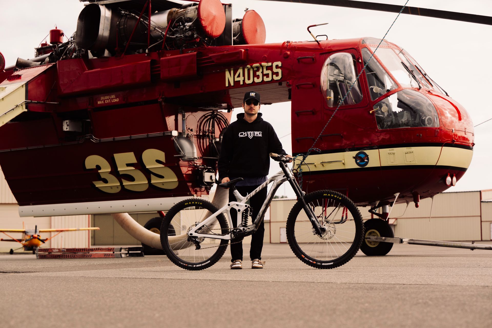 Man standing with a mountain bike in front of a red helicopter, overcast day.