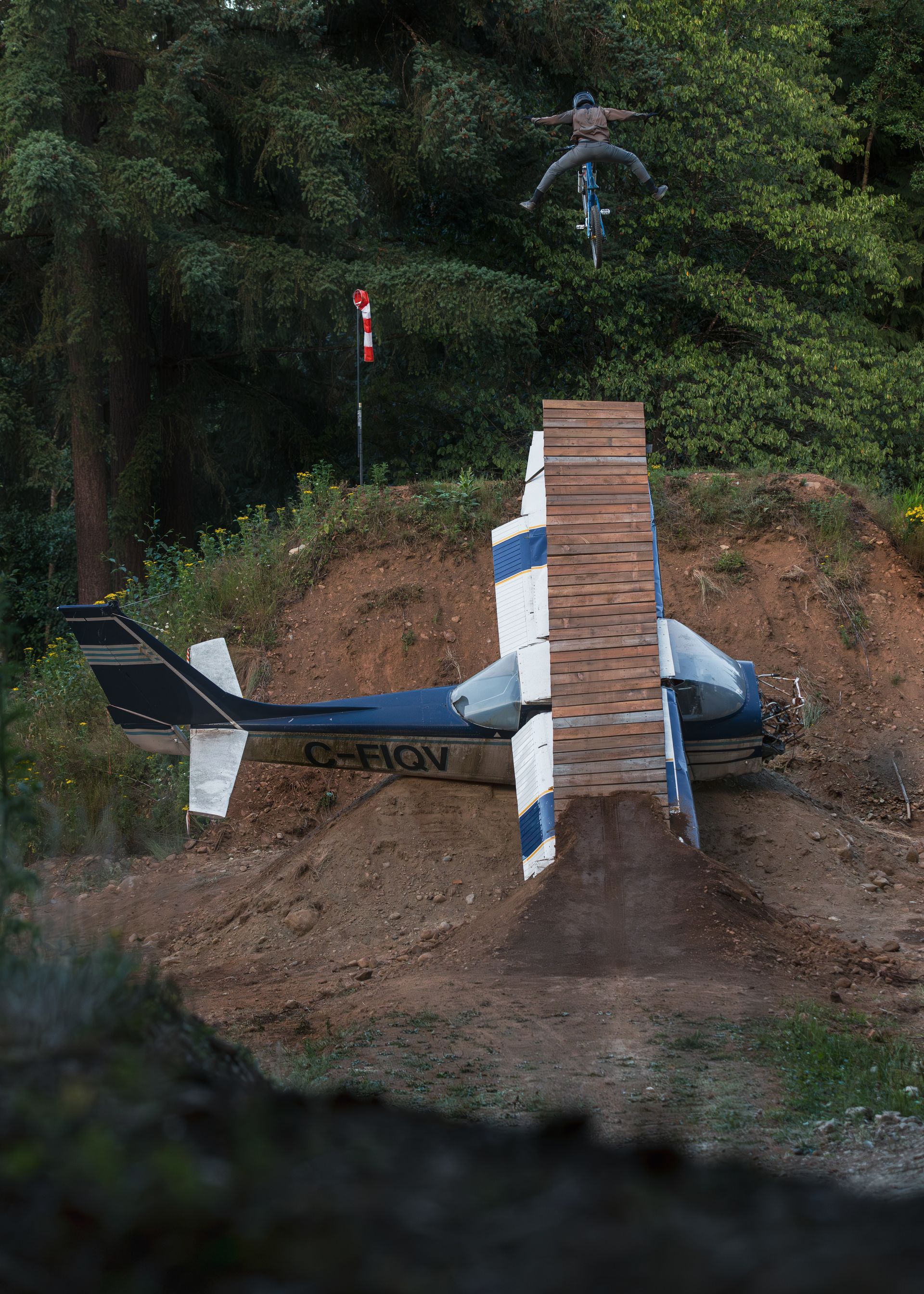 A person on a bike jumps over a helicopter ramp built into a dirt hill.