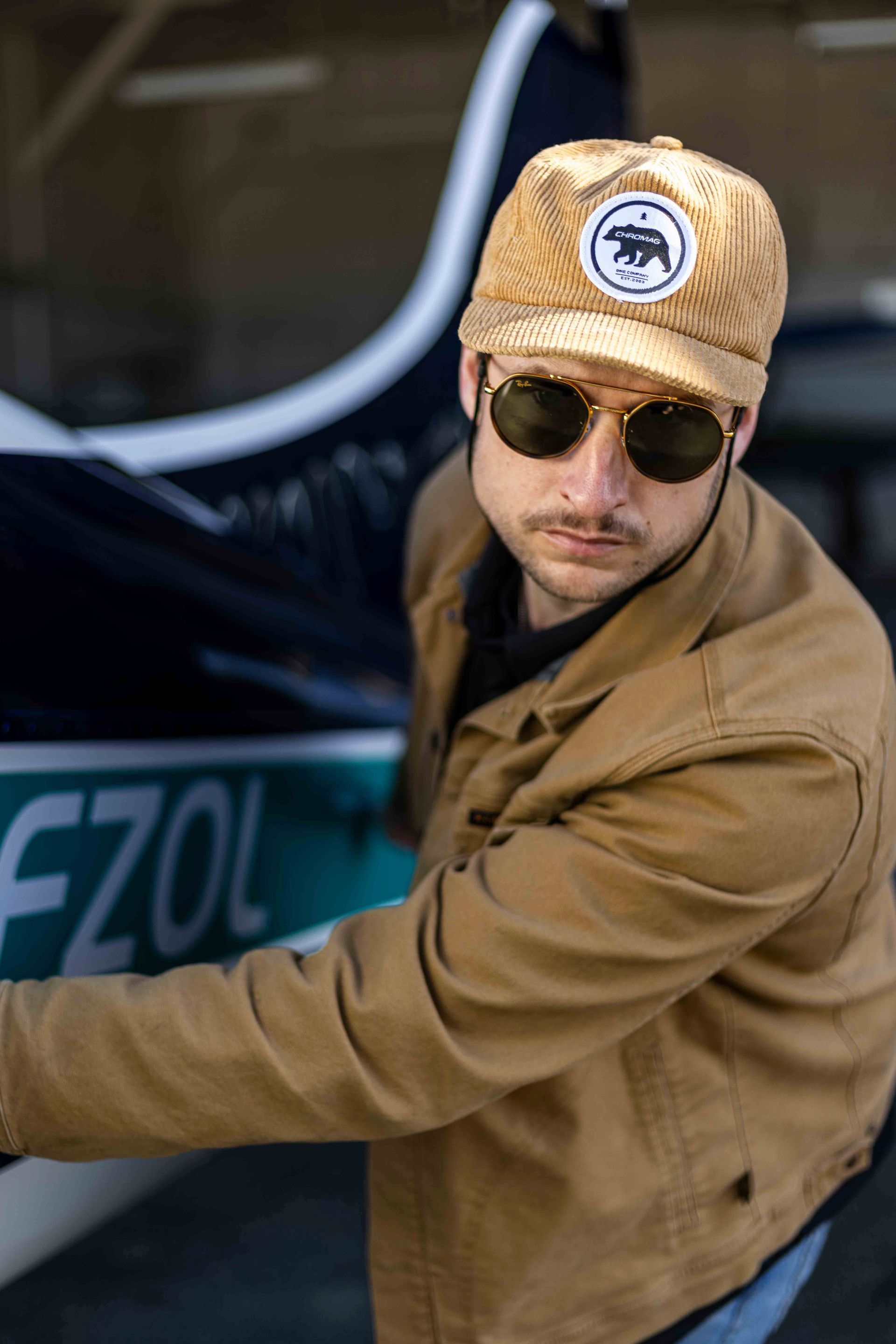 Man wearing sunglasses and hat, holding onto a plane's wing.
