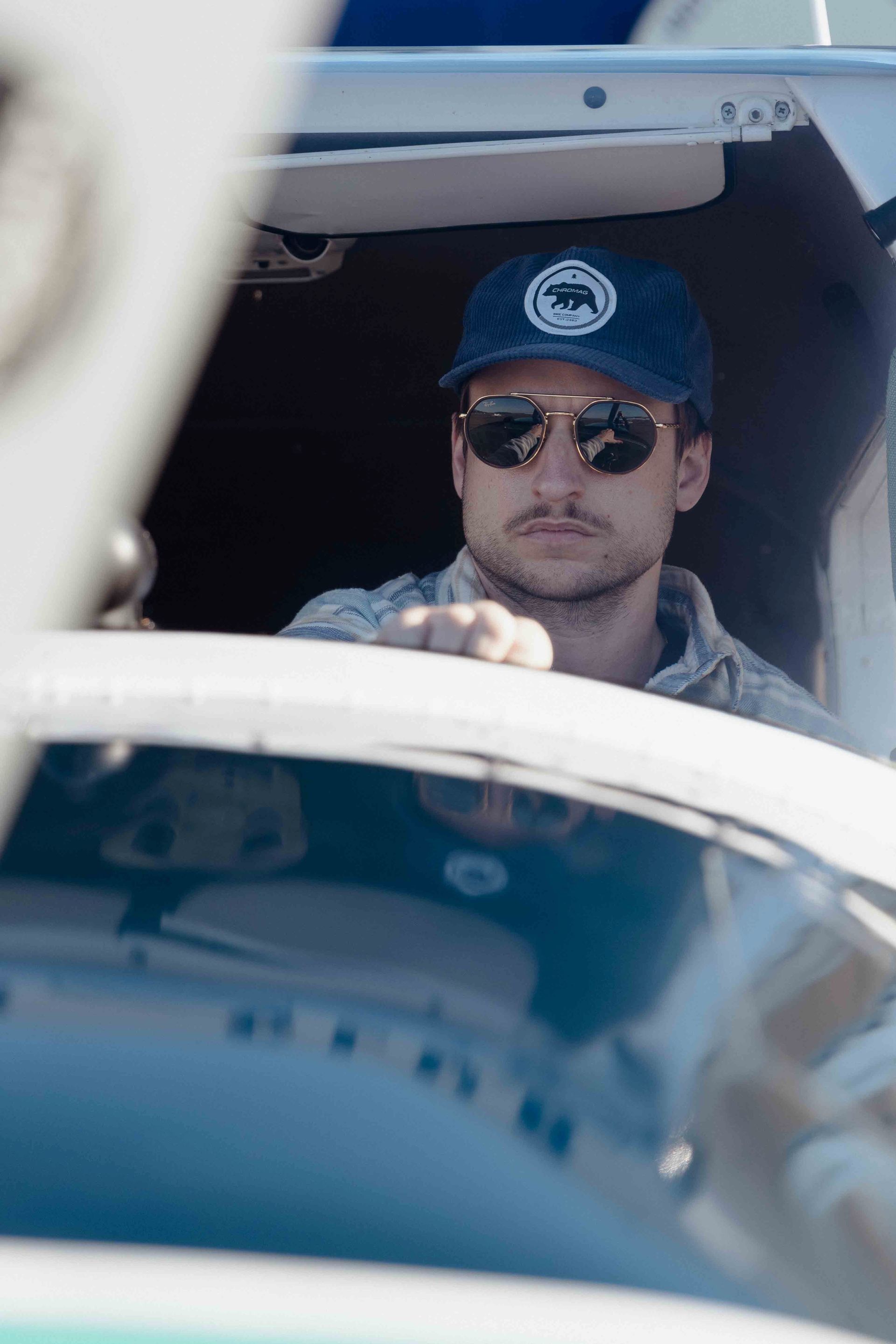 Man in sunglasses and baseball cap in the cockpit of a small plane.