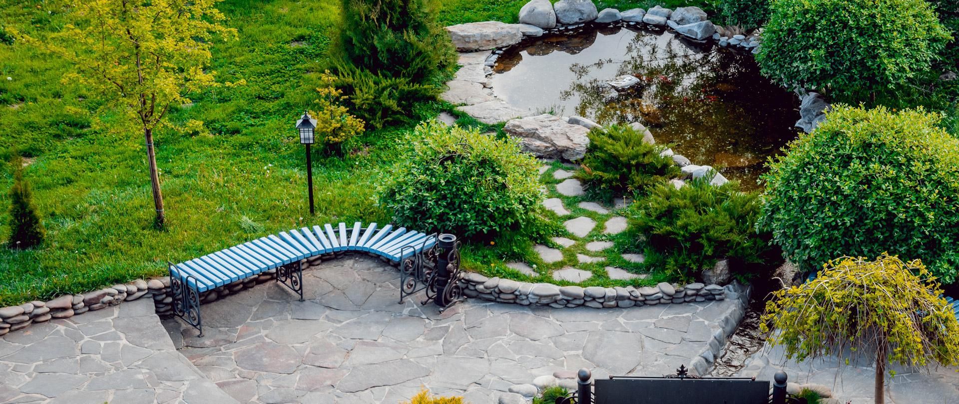 Banc incurvé au bord d'un petit étang paysager avec rochers, herbe et arbres