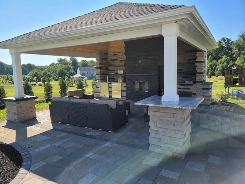 Outdoor pavilion with fireplace, seating, and bar area, on a stone patio.