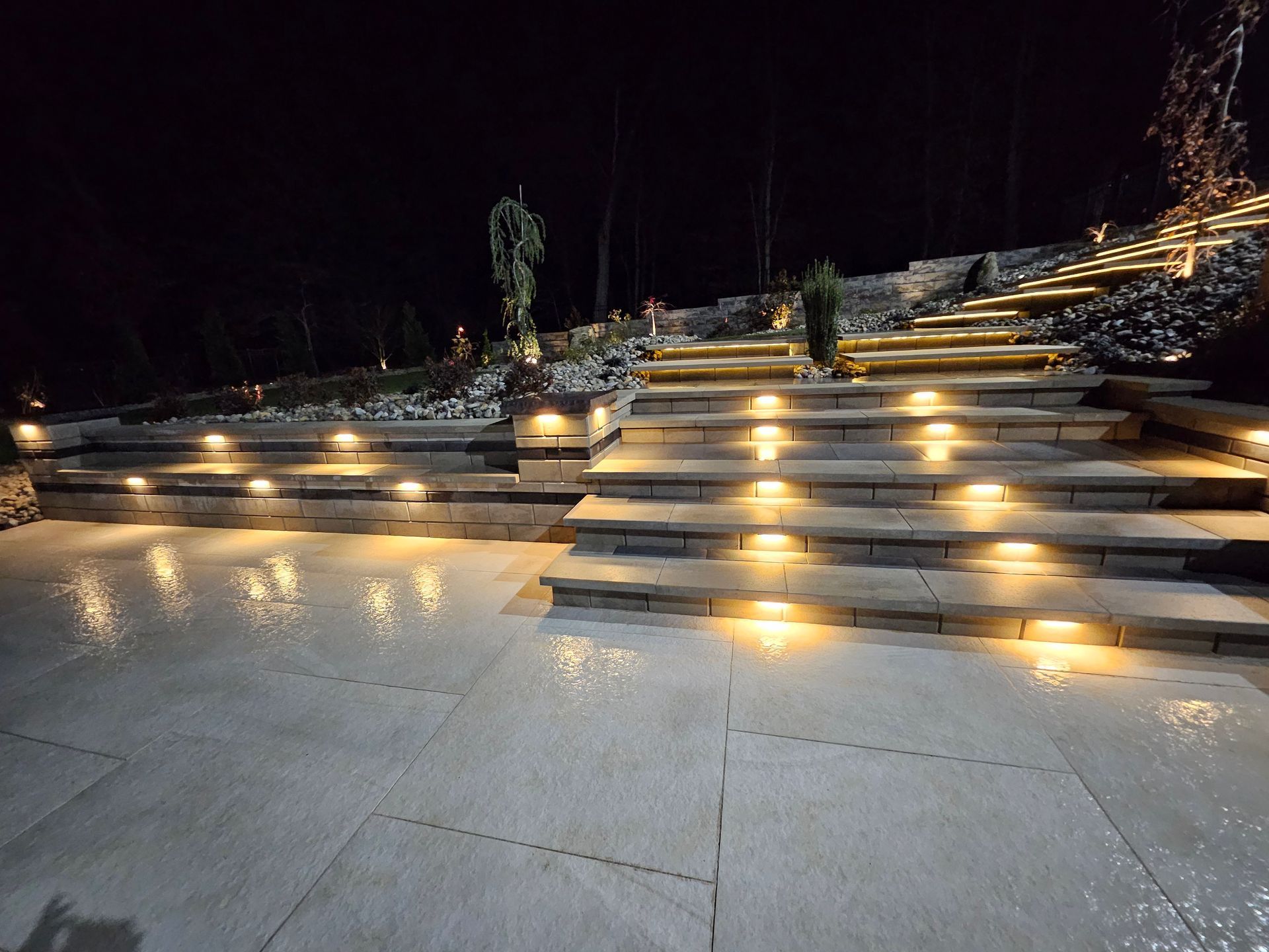 Nighttime view of a patio with a fireplace, grill, and seating area illuminated by warm lighting.