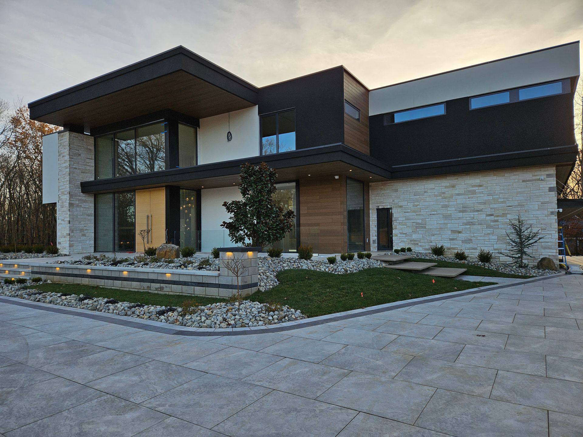 A modern, two-story home with light stone, dark wood, and black siding, featuring a paved driveway and landscaped yard.