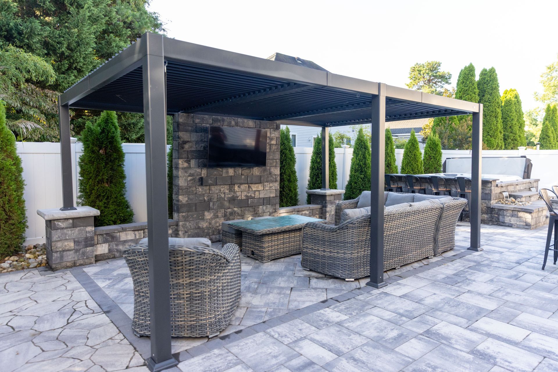 Backyard with stone patio, pergola, and elevated deck on a multi-level landscape, with a large house.