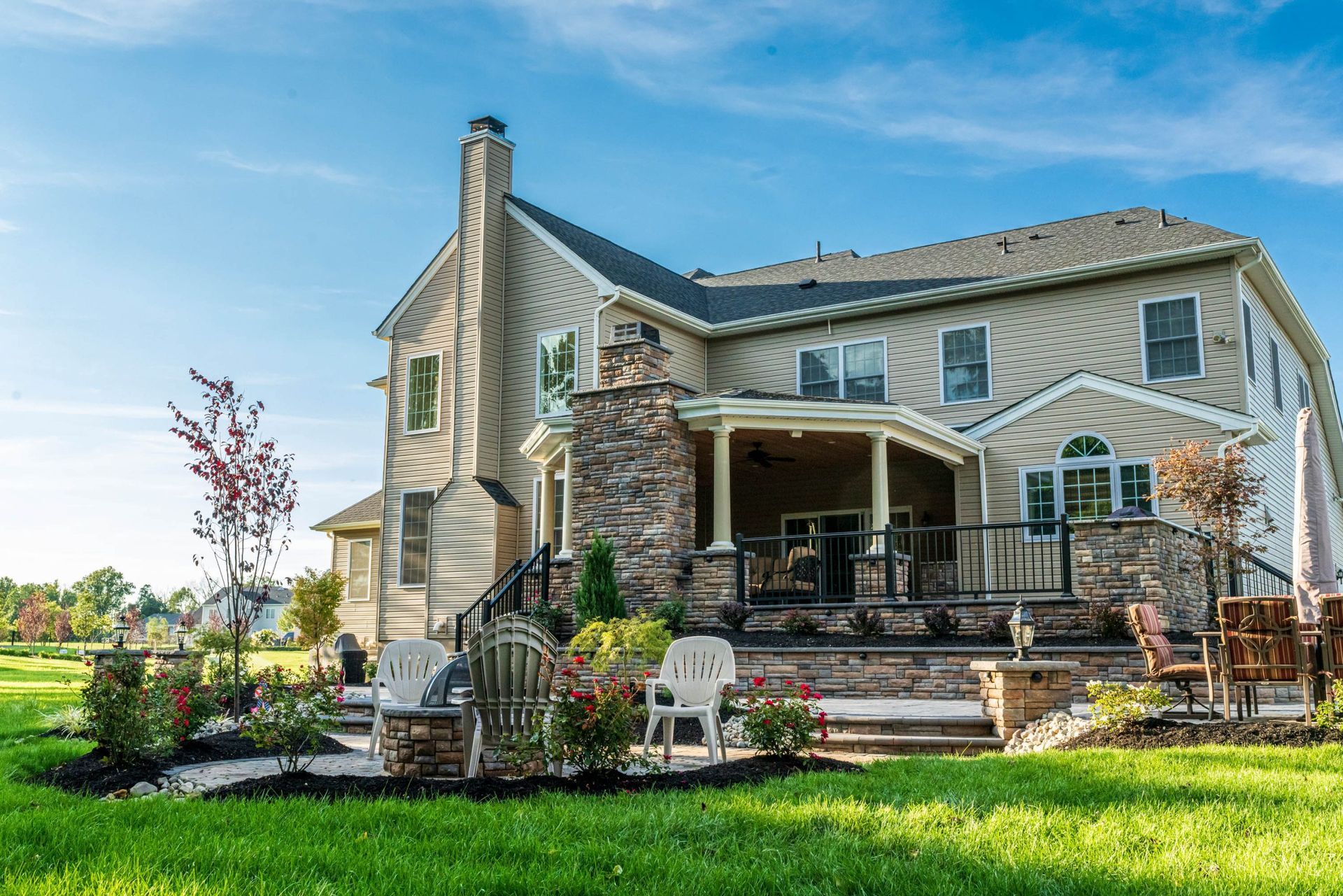 Large house with stone patio, green lawn, and blue sky.