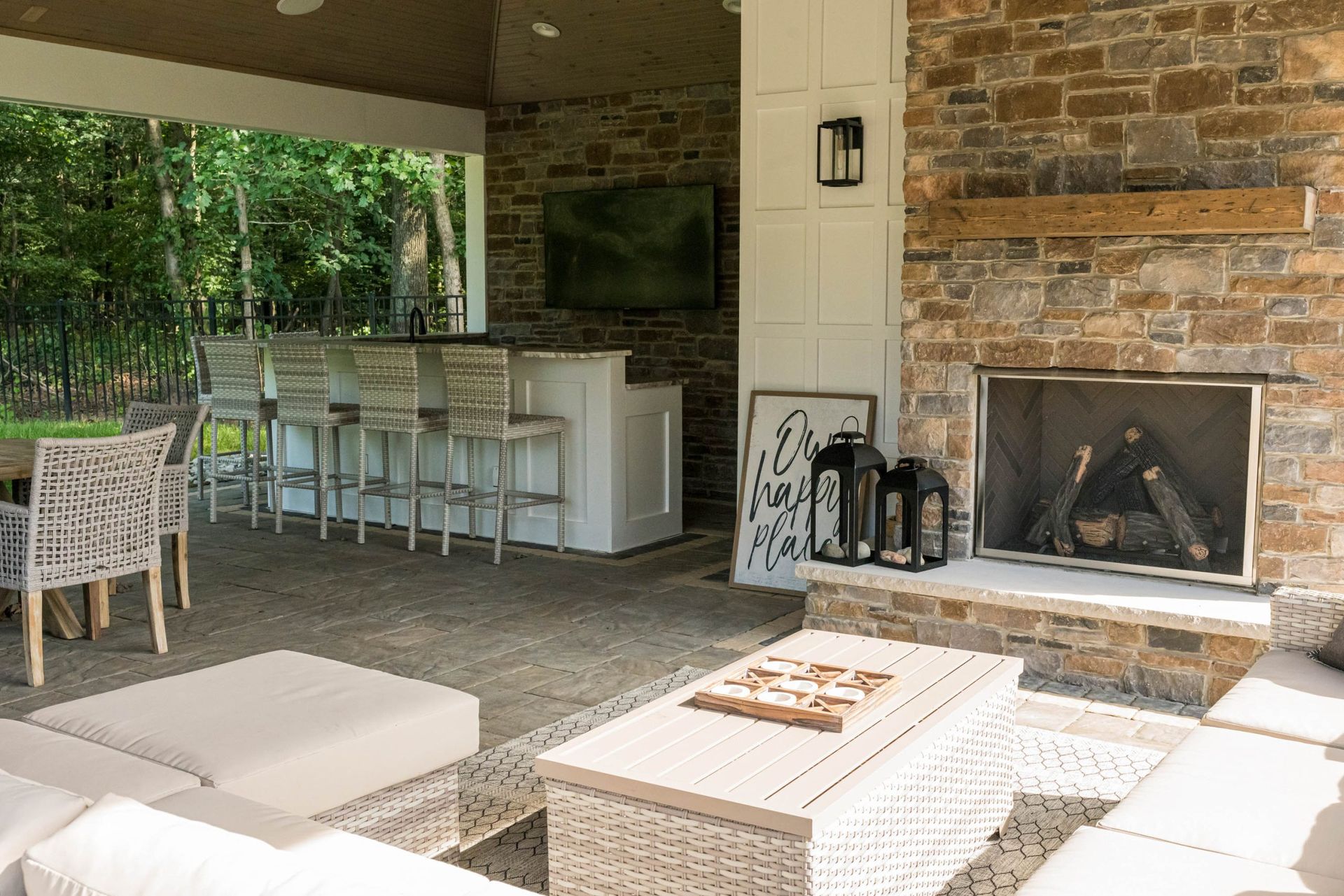 Outdoor patio with a bar, seating, fireplace, and TV. Stone and white accents.