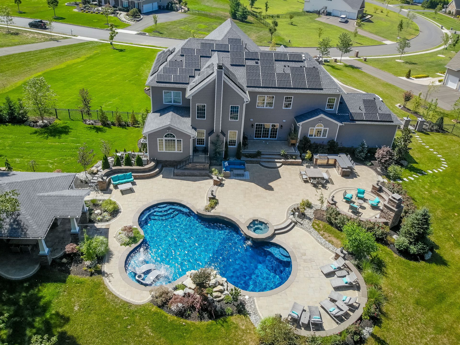 Aerial view of a large gray house with a pool, patio, and outdoor seating on a grassy property.