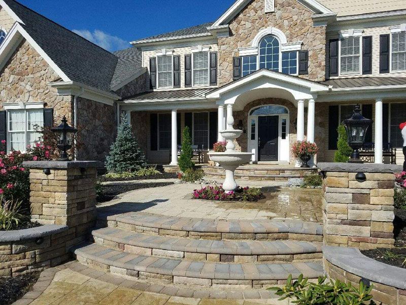 Stone-clad home with a tiered entrance. A fountain sits on the porch, flanked by lanterns and landscaping.