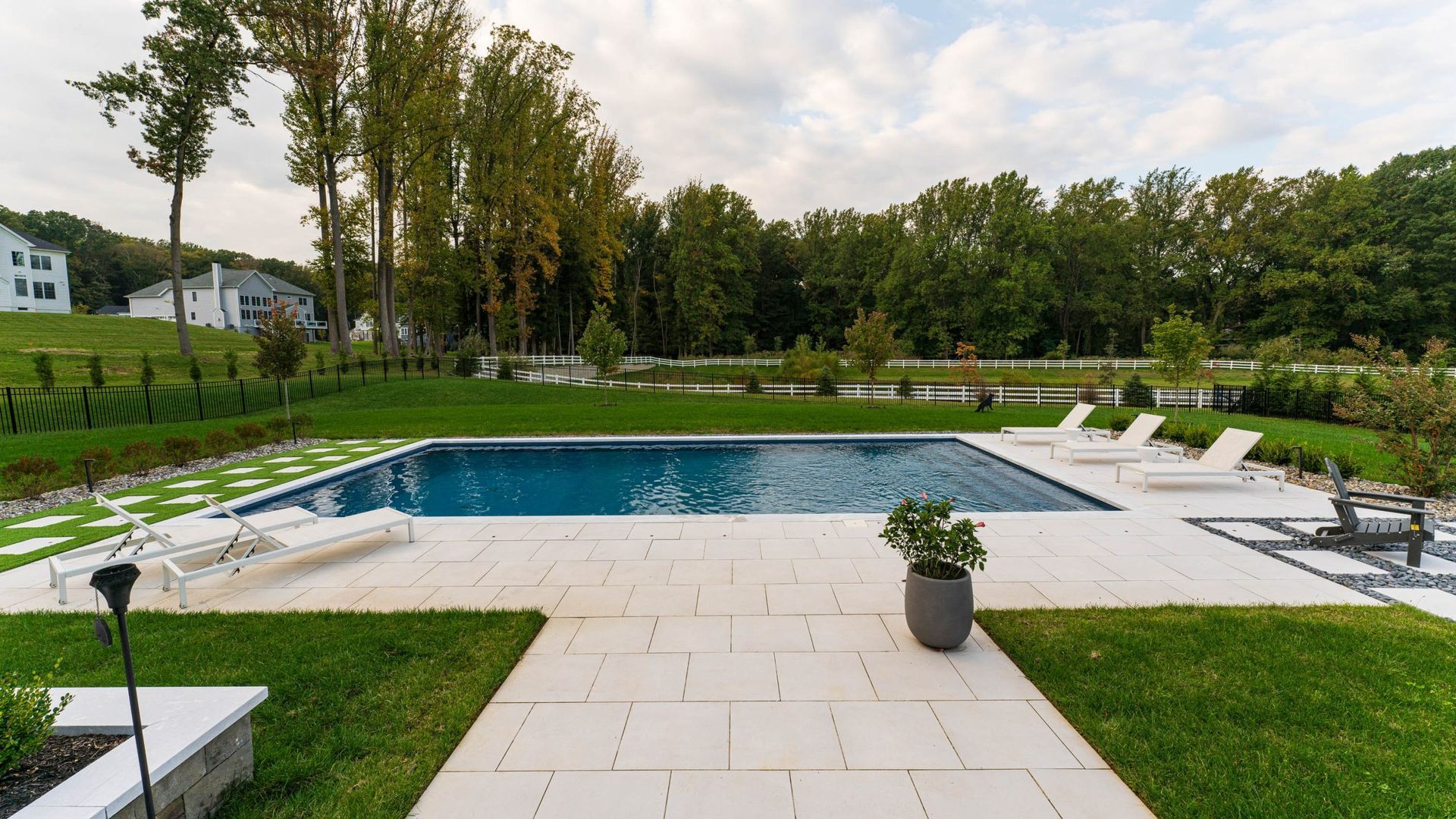 Rectangular pool in a modern backyard with lounge chairs and green lawn.