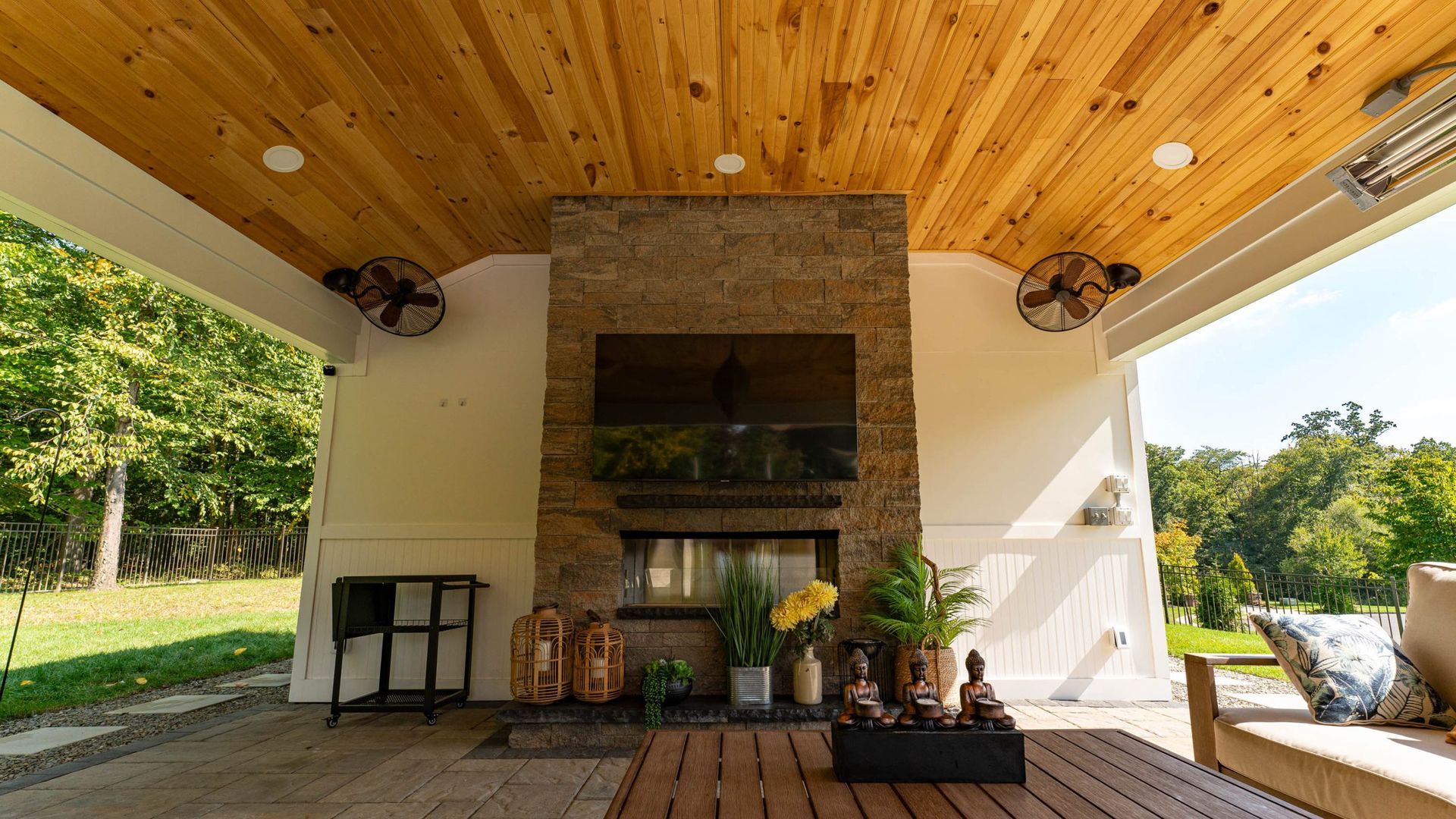 Covered patio with fireplace, TV, wood ceiling, fans, and outdoor furniture.