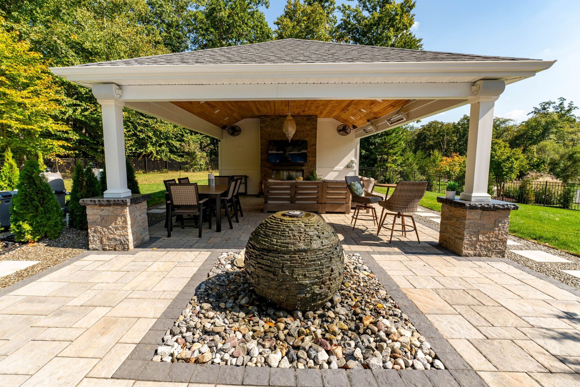 Outdoor patio with stone pavers, pergola, seating, and water fountain.