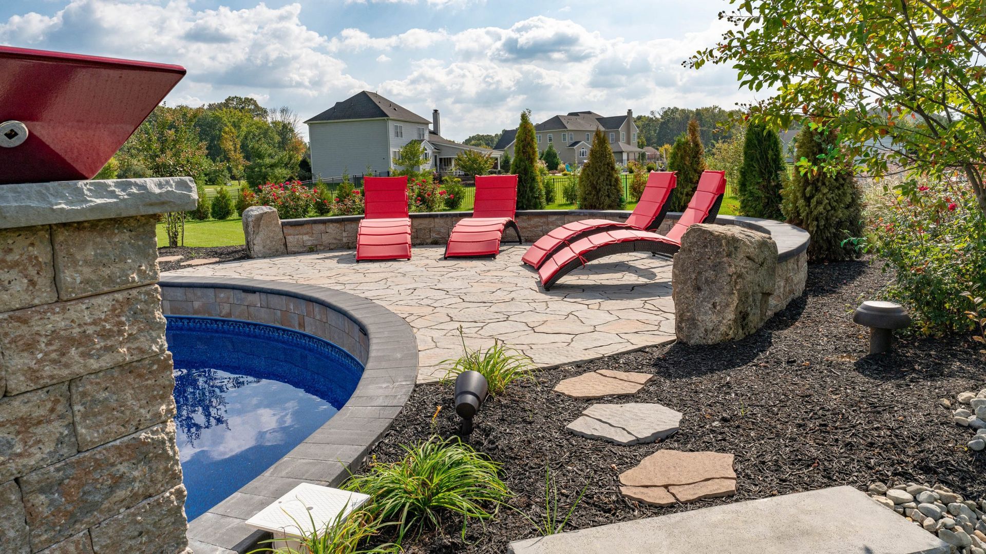 Poolside patio with red lounge chairs, stone path, and manicured landscaping.