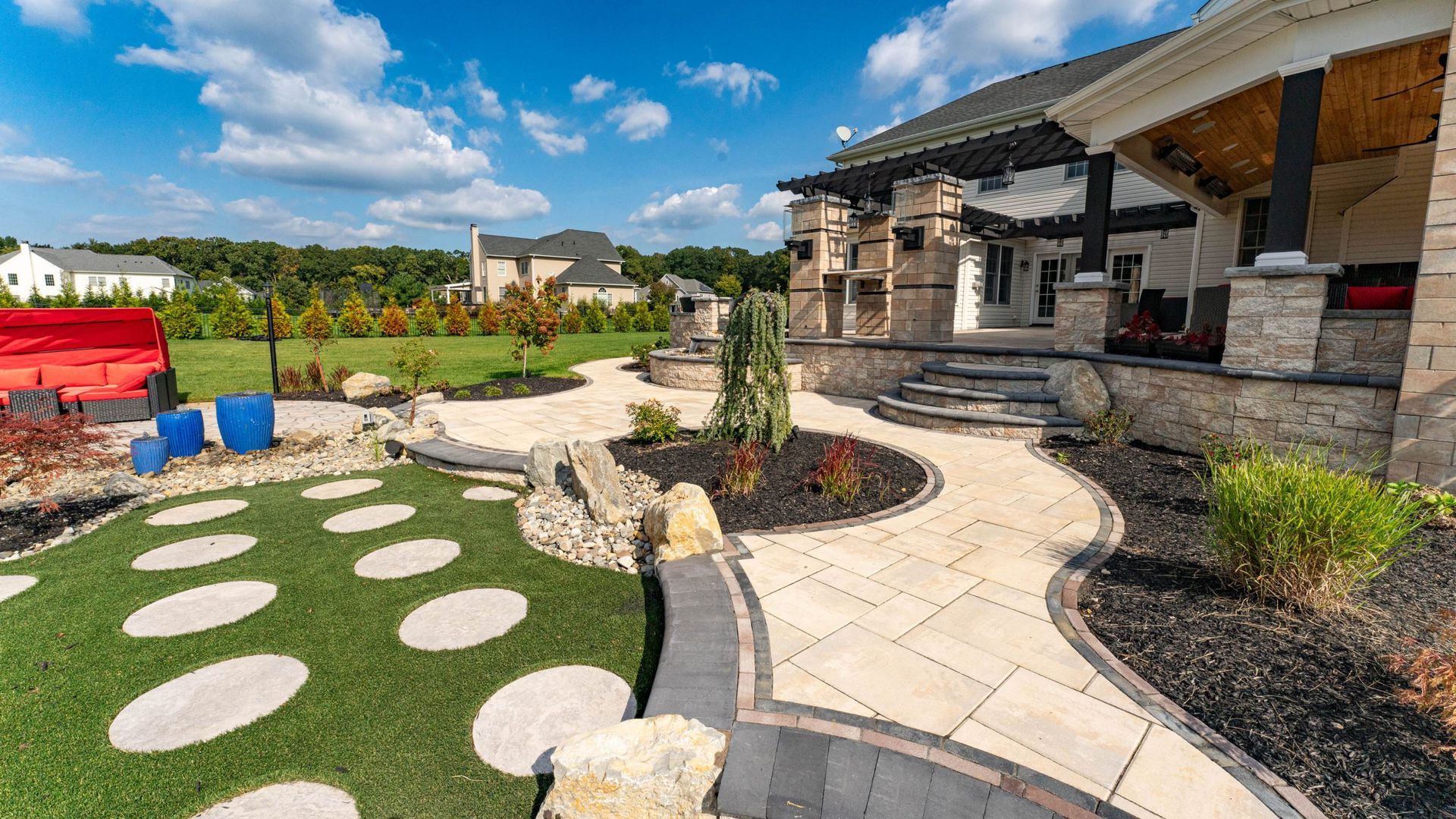 Outdoor patio with curved stone walkway and stepping stones in a manicured yard under a blue sky.