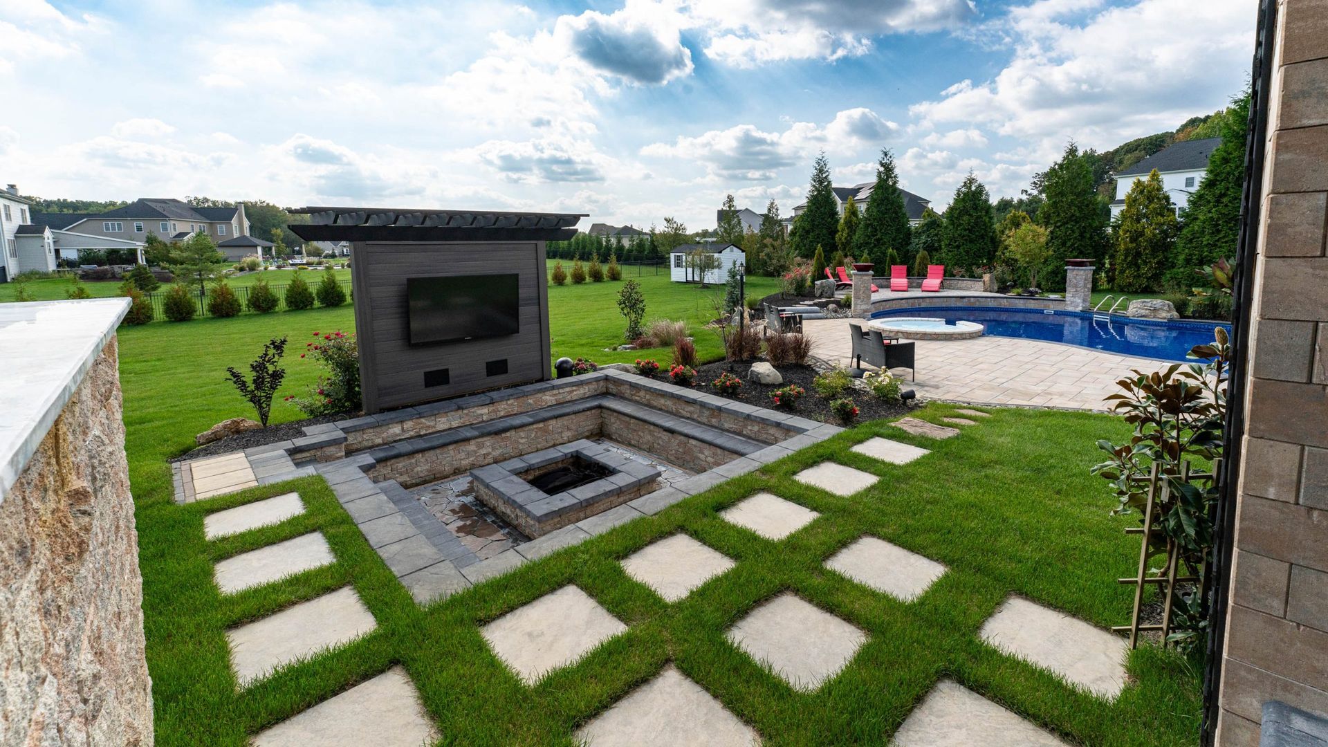 Outdoor living space with fire pit, television, swimming pool, and green lawn.