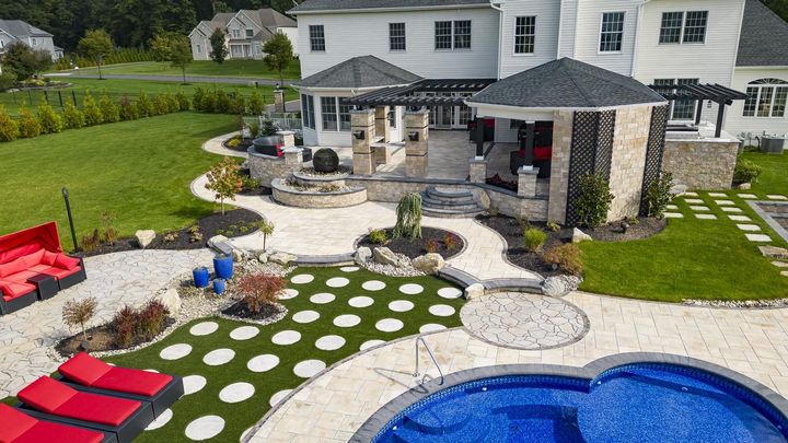 Luxurious backyard with pool, seating, stone patio, gazebo, and green lawn.