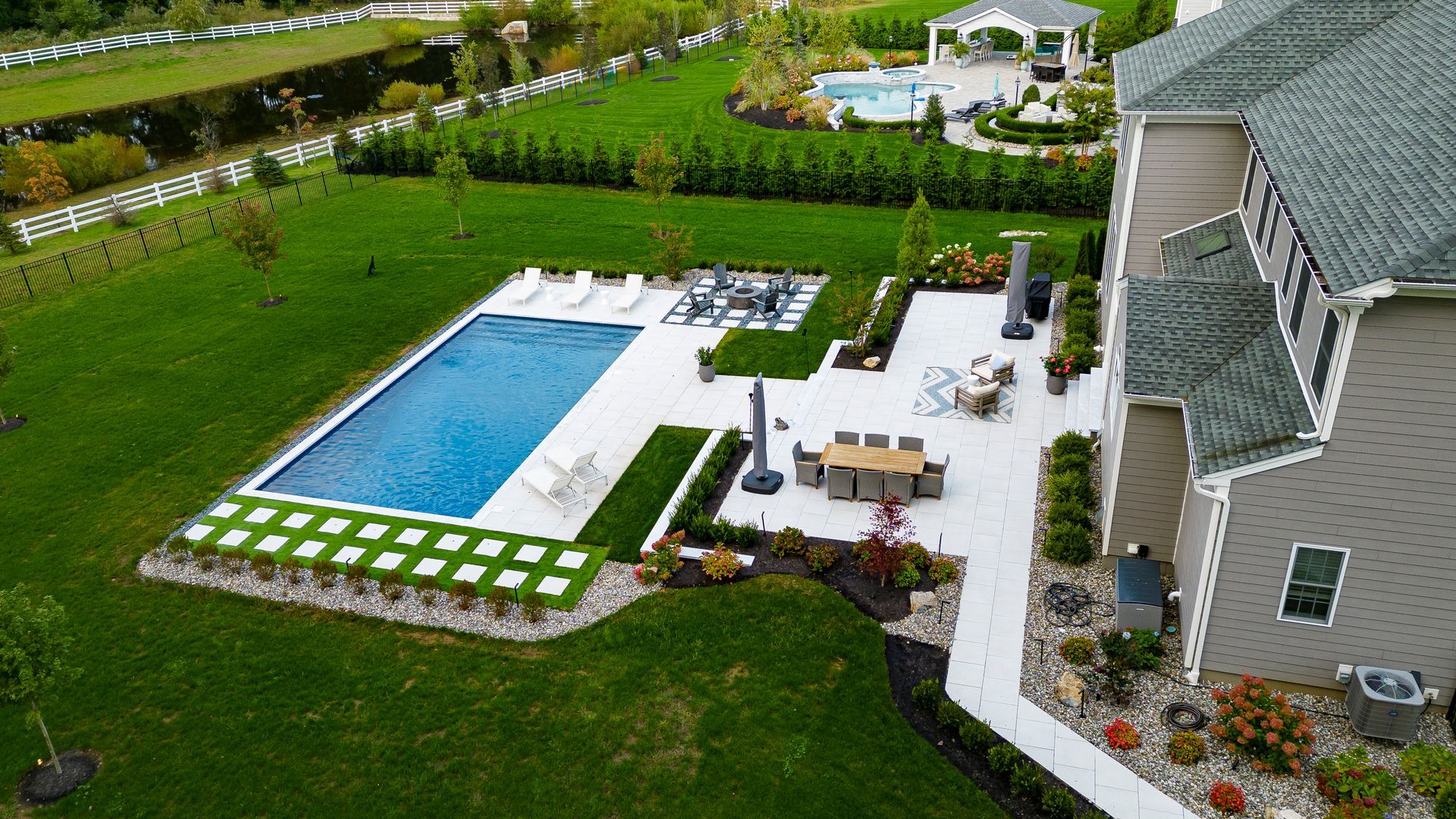 Aerial view of a luxury backyard with a rectangular pool, patio, and lush landscaping.