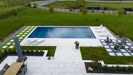 Backyard pool with white patio, lawn, trees, and lounge chairs.