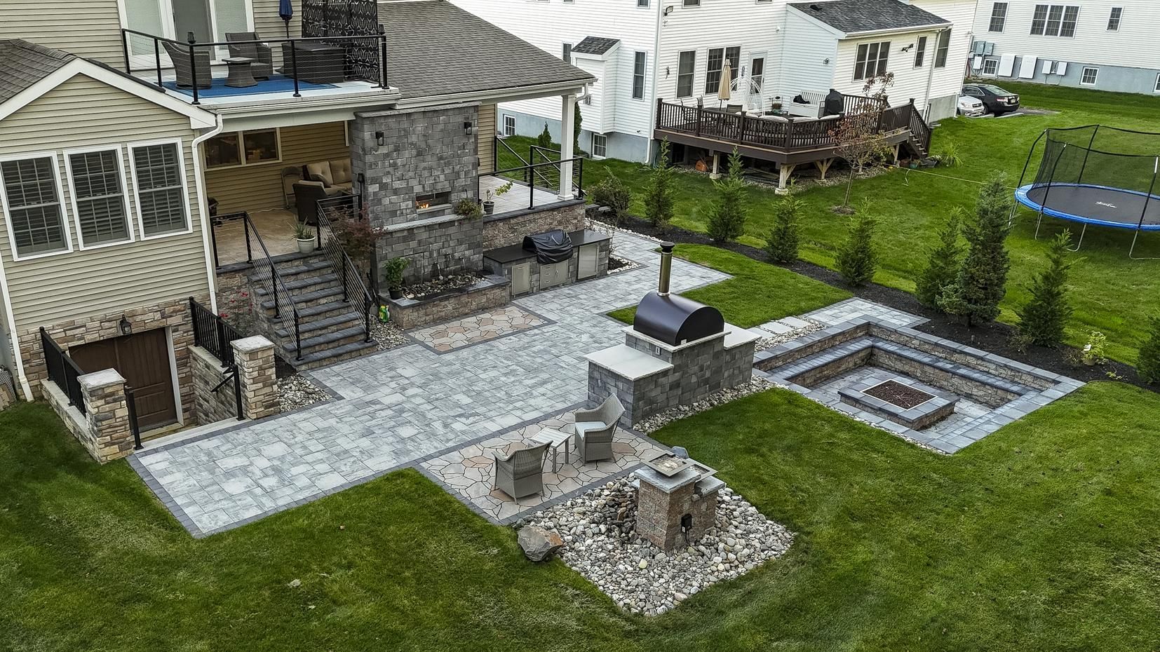 Backyard patio with stone work, outdoor kitchen, fire pit, and trampoline.