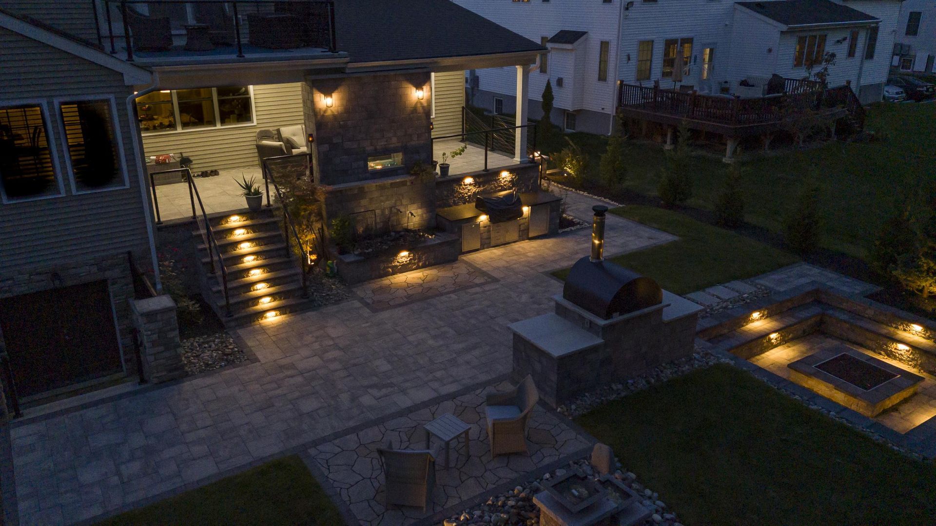 Nighttime view of a patio with a fireplace, grill, and seating area illuminated by warm lighting.