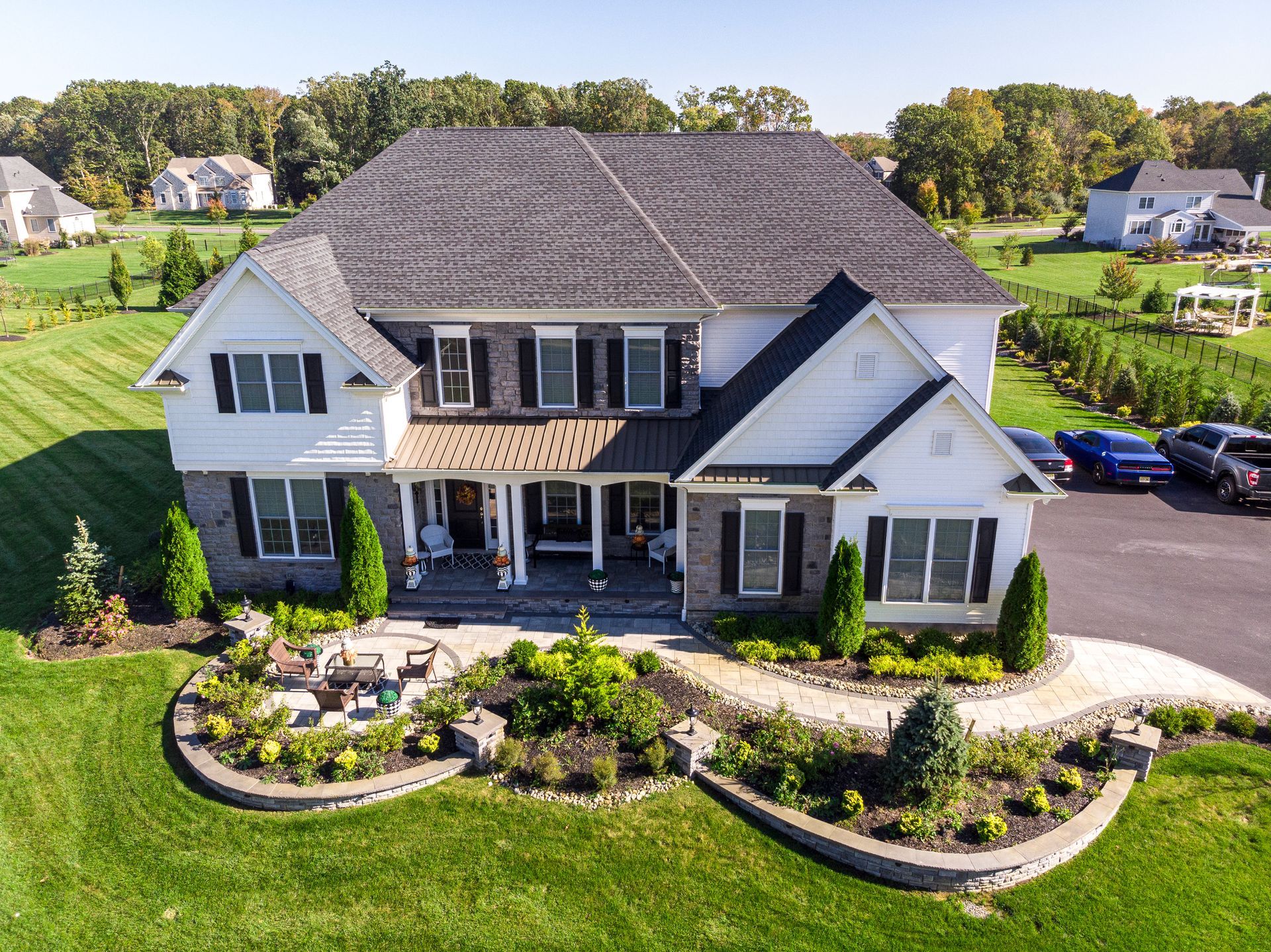 Two-story white house with gray roof and black shutters, landscaped front yard, sunny day.