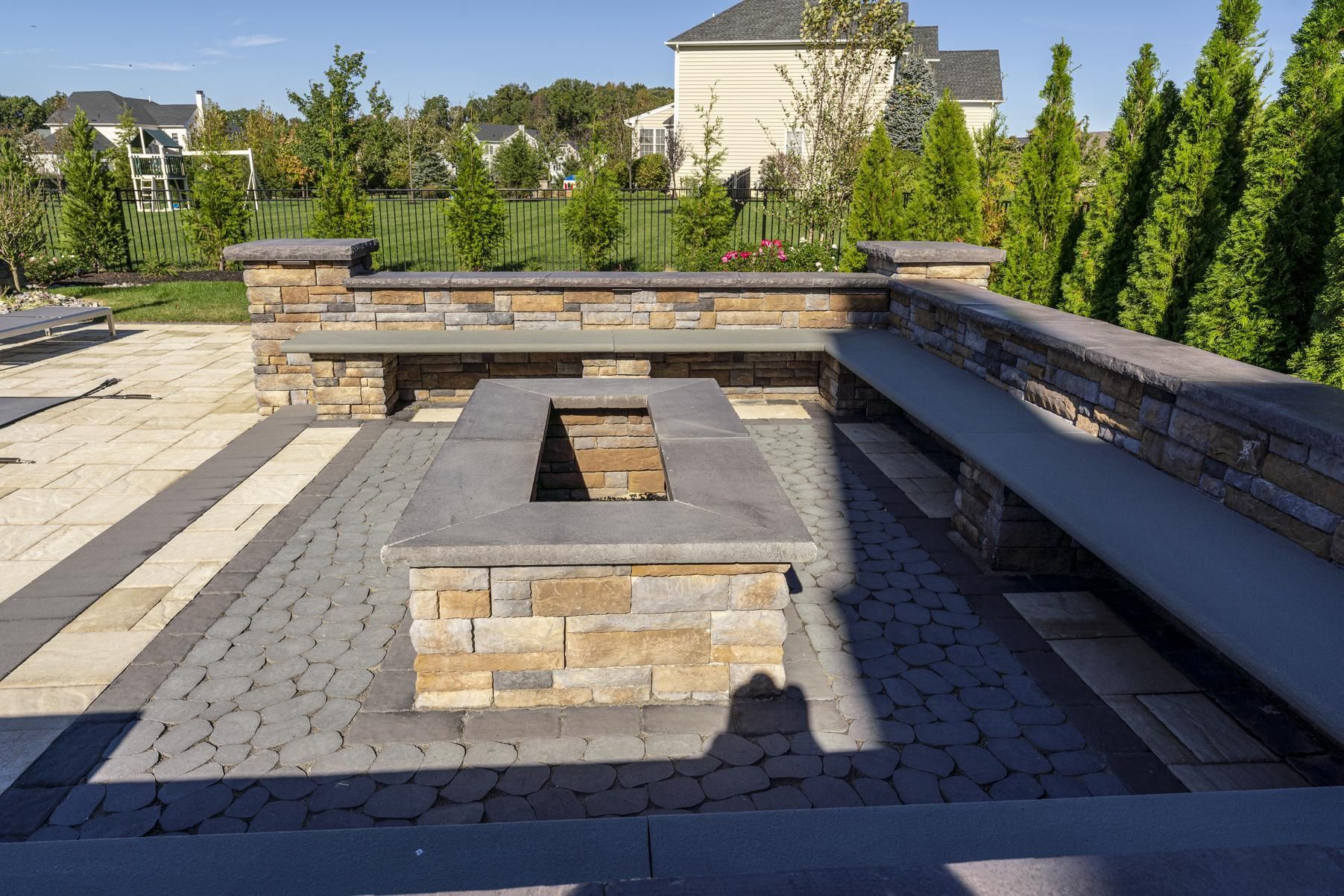 Stone fire pit with built-in seating on a paved patio, surrounded by stone walls and greenery.