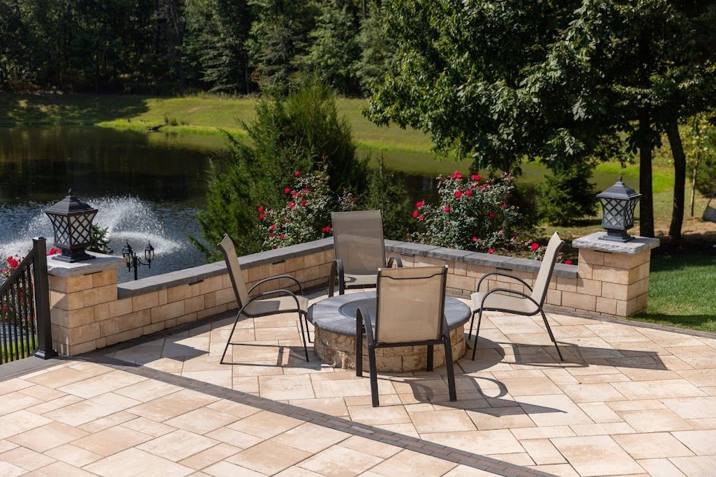 Patio with fire pit, seating, and pond view, surrounded by greenery and stone walls.