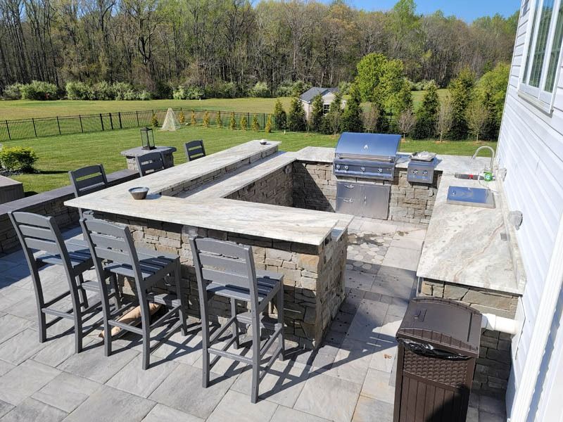 Outdoor kitchen with stone counters, a grill, sink, and bar seating.