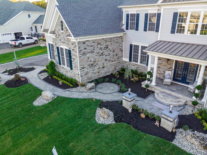 Aerial view of a gray two-story house with stone accents, landscaped yard, and paved walkway.