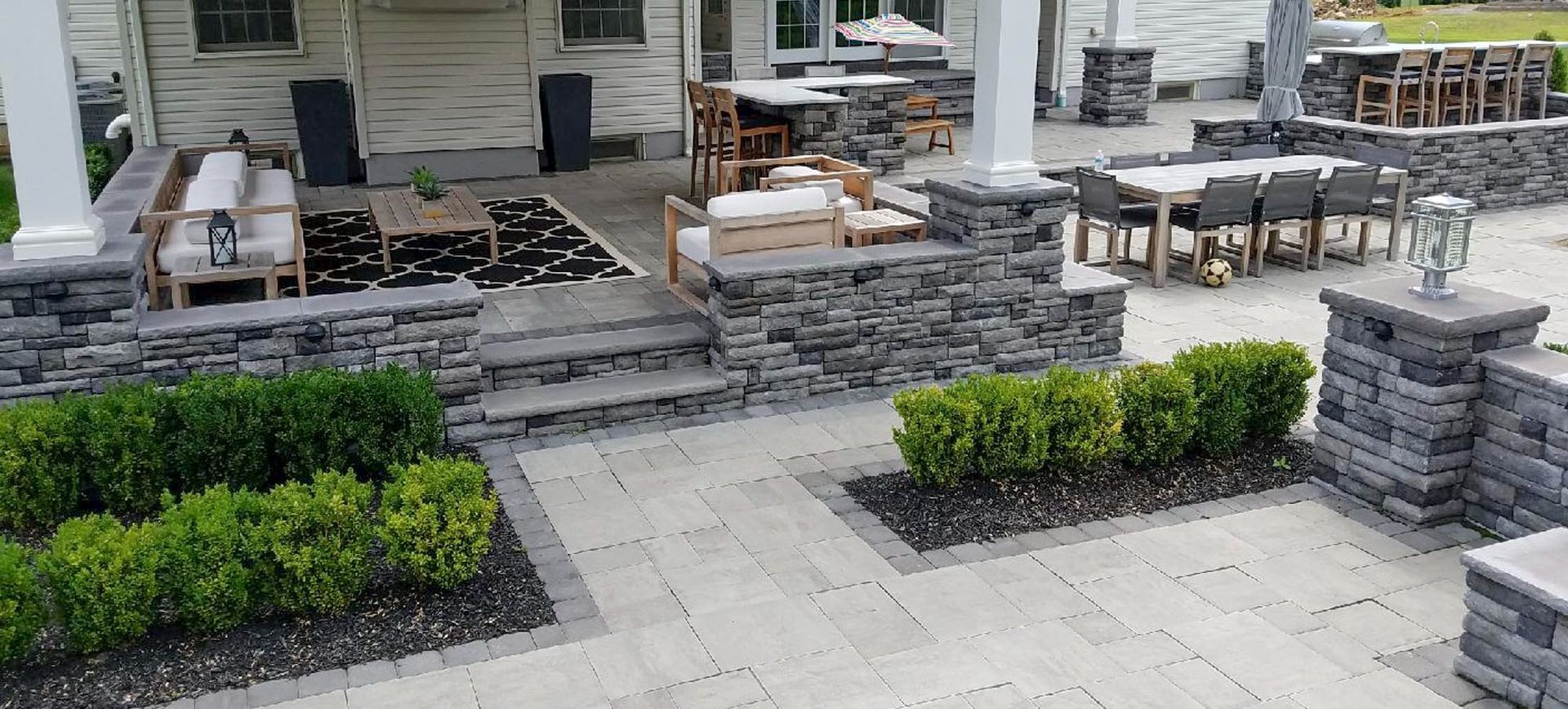 Outdoor patio with stone walls, furniture, greenery, and dining area.