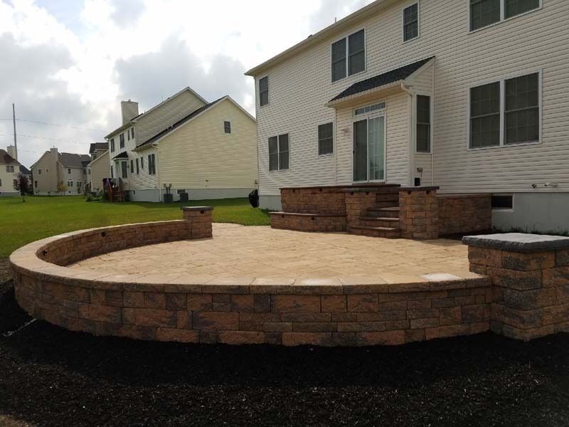 A brick patio with curved retaining wall and steps leading to a house with white siding.