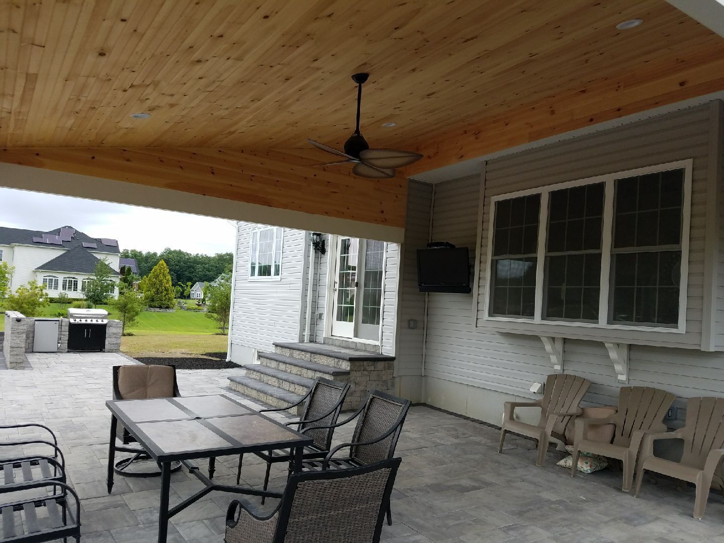 Patio with wooden ceiling, fan, furniture, barbecue, and house with windows.