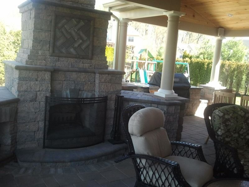 Outdoor stone fireplace and seating area on a patio, with a playground in the background.