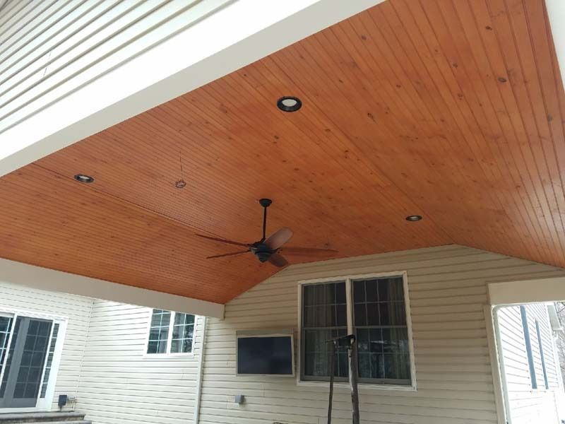 Wooden patio ceiling with recessed lights and ceiling fan. Beige siding and windows visible.