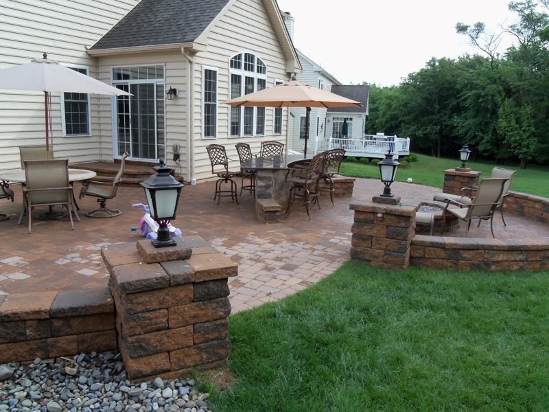 Patio with tables, chairs, and umbrellas next to a house with a green lawn.