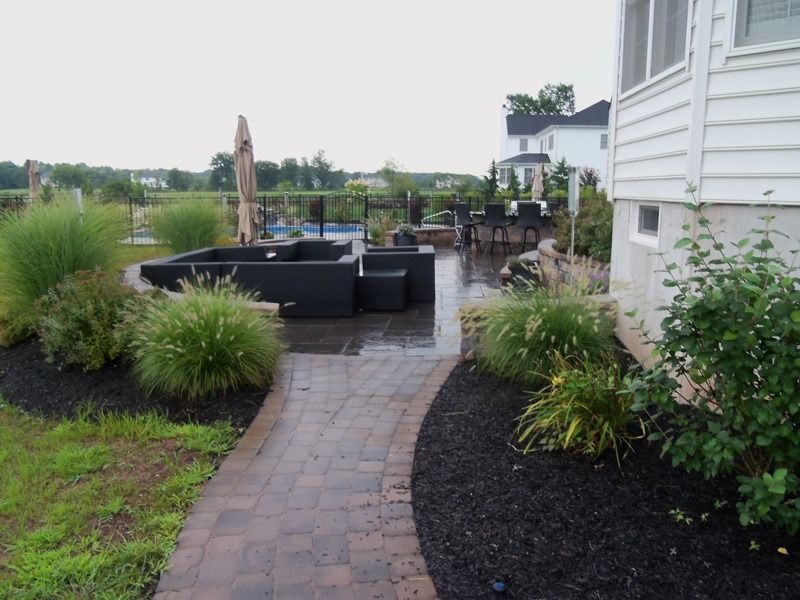 Brick pathway leading to patio with black furniture and landscaping.