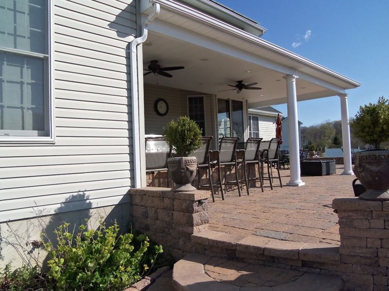 Covered patio with seating, stone steps, potted plants, and the side of a house.
