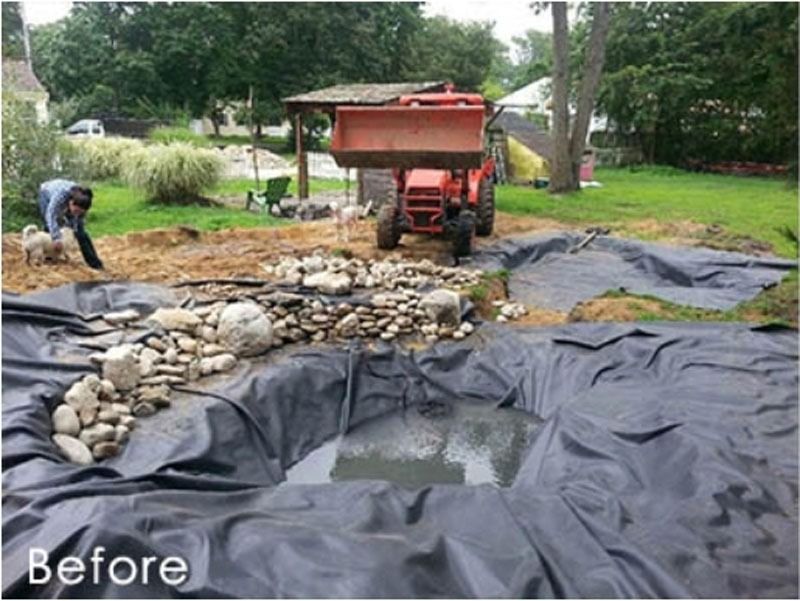 Man constructing a pond, tractor with a load of soil, rocks, tarp, in a yard.