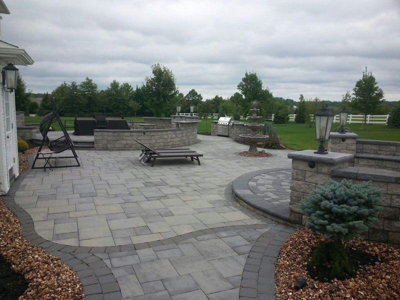 Patio with brick pavers, outdoor kitchen, fountain, and seating area under cloudy sky.