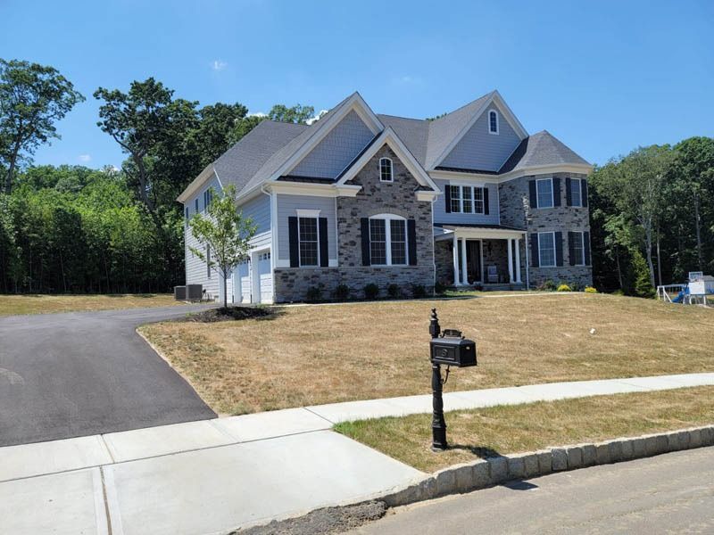 Two-story house with blue siding, stone accents, black shutters, and a lawn with a black mailbox in front.