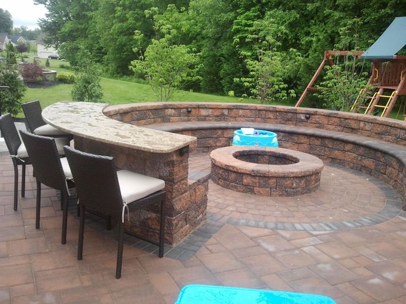 Brick patio with a curved fire pit, built-in seating, and bar. Four chairs are positioned at the bar.