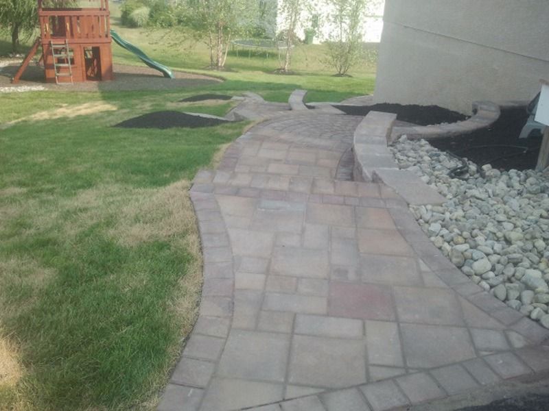 Stone path curves along a house and grassy yard.  Play structure visible in the background.