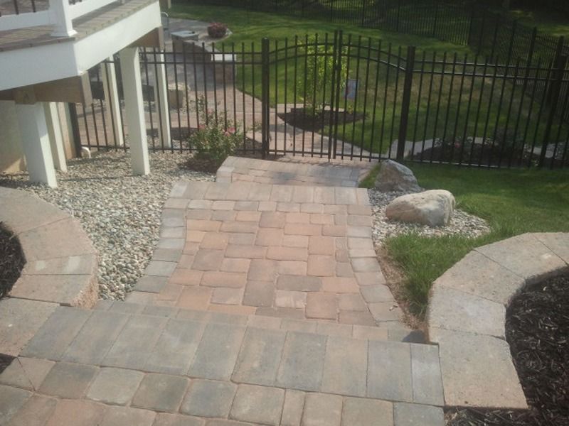 Stone steps leading to a black fence, surrounded by landscaping, under a deck.