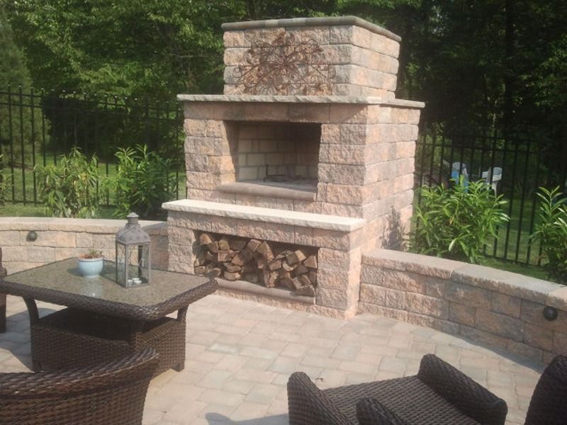 Stone outdoor fireplace with wood storage and patio seating.