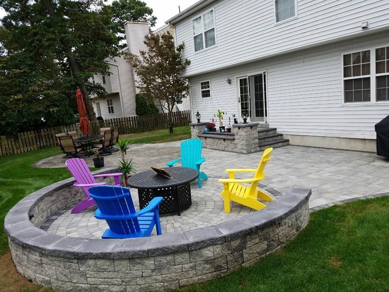 Backyard patio with colorful Adirondack chairs around a fire pit, next to a house.