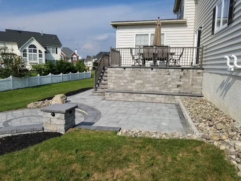 Backyard patio with raised deck, stone wall, and circular fire pit.