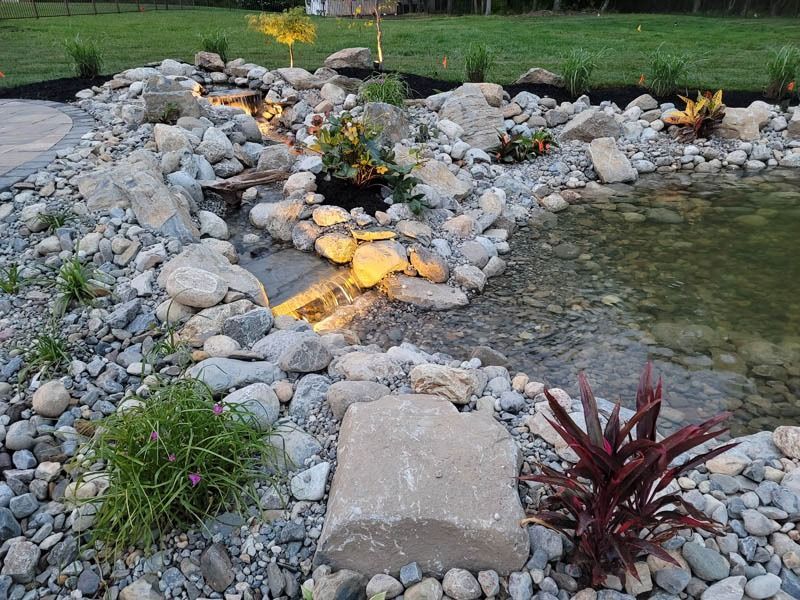 Rock garden with a stream and small waterfall; lit by spotlights at night.