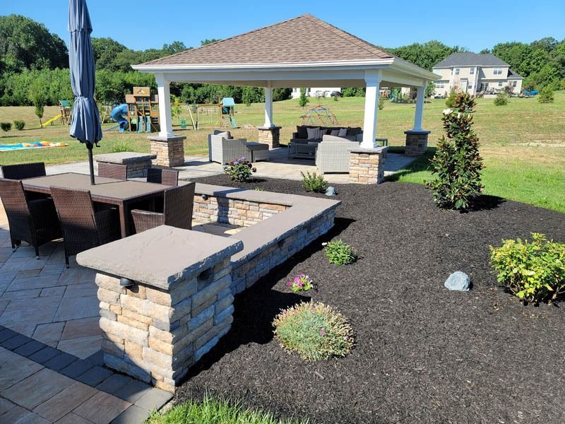 Outdoor patio with gazebo, seating area, fire pit, and dining table on a sunny day.