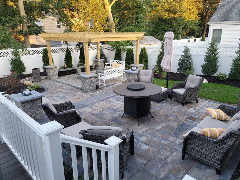 Patio with seating, fire pit, and pergola under a sunny sky.