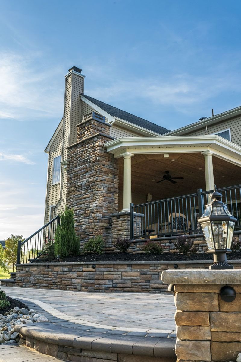 Stone house with covered patio, chimney, and landscaped yard.
